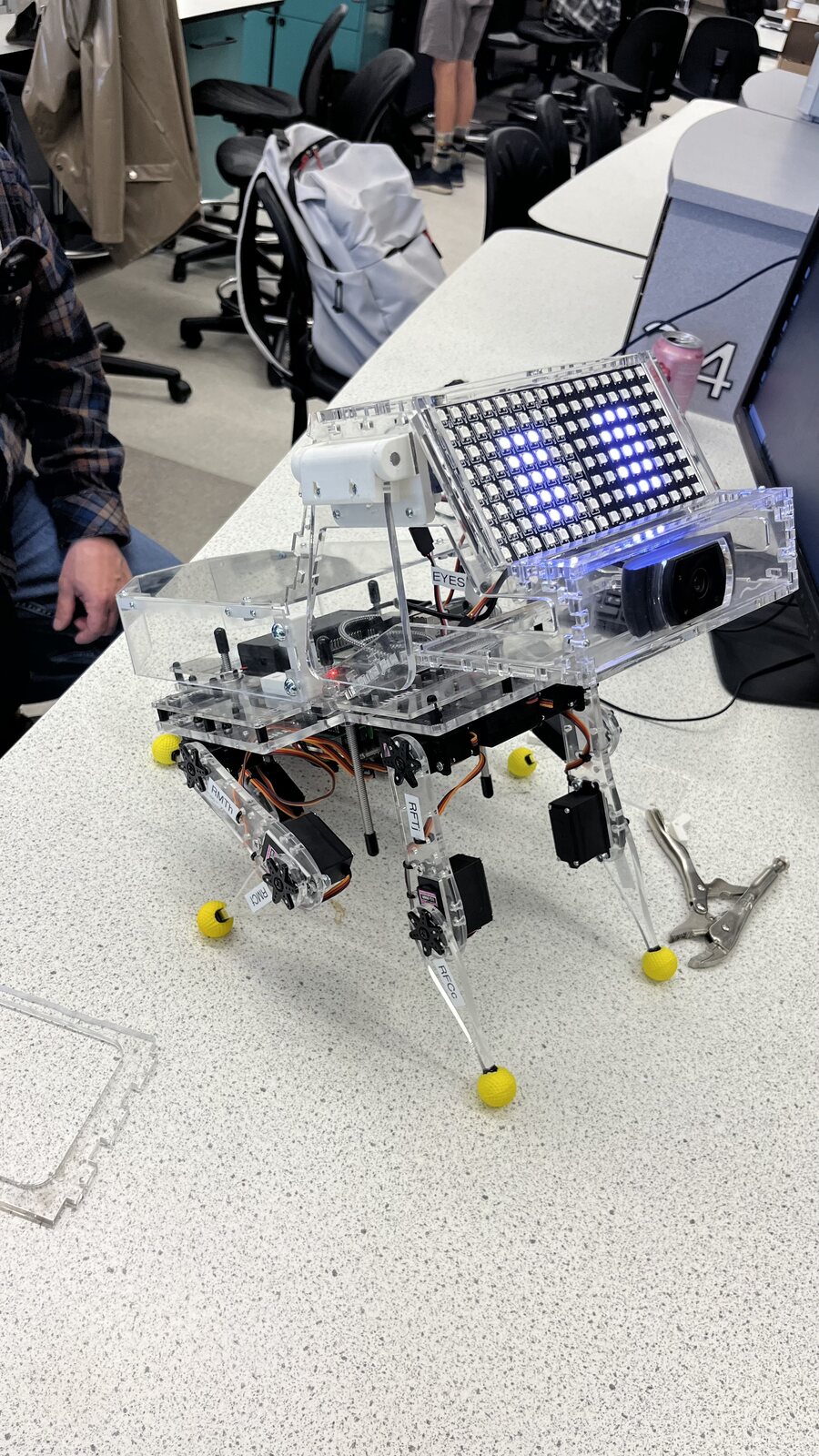 Physical Sox prototype with clear acrylic body, camera, LED eye panel, and labeled servo legs